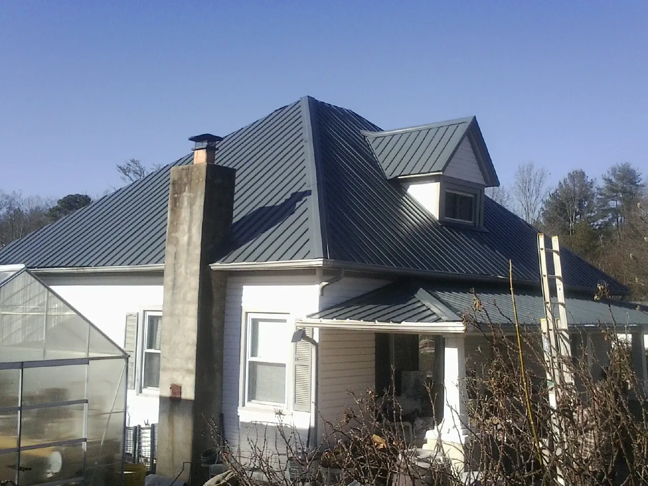 Dark blue standing seam metal roof on a white farmhouse with dormer — Slate & Tile Roof Repair by Roofing Brothers in Hume