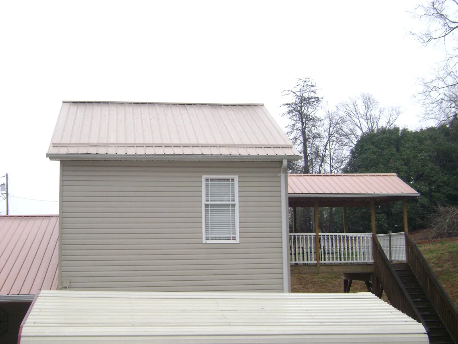 Tan metal roofs on a two story addition and attached porch, from a Roof Replacement job in Hume
